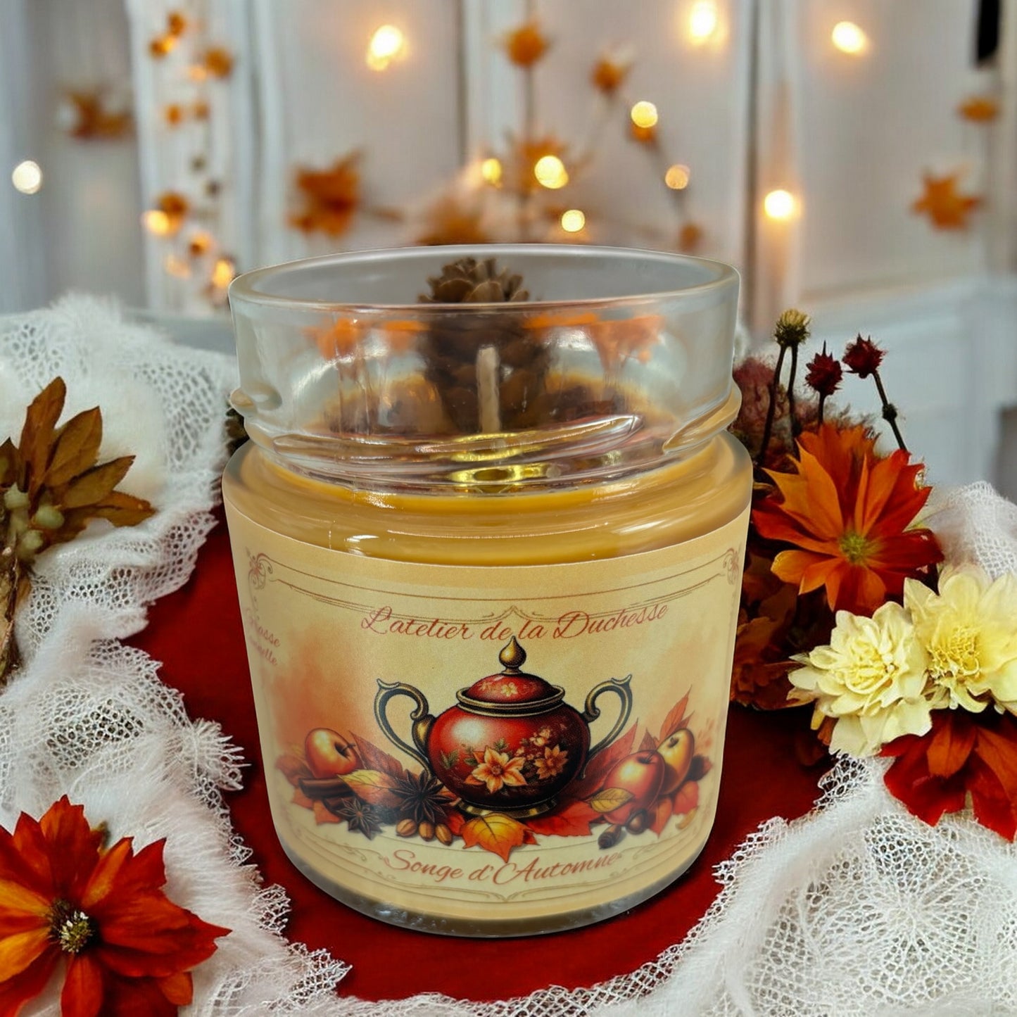 Glass candle labeled 'Songe d'Automne' surrounded by autumn flowers and warm lights.