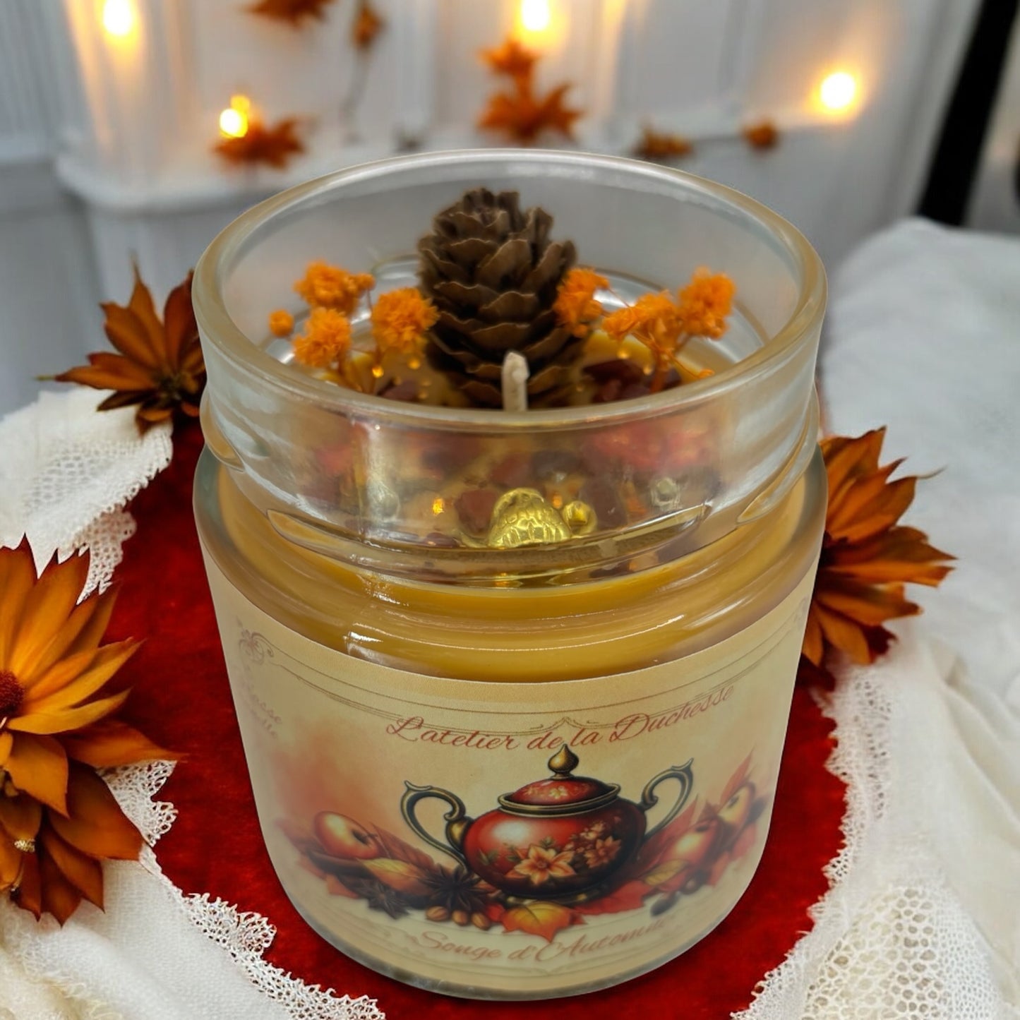 Bougie Songe d’automne with pinecone and floral decorations in a glass jar surrounded by autumn leaves.