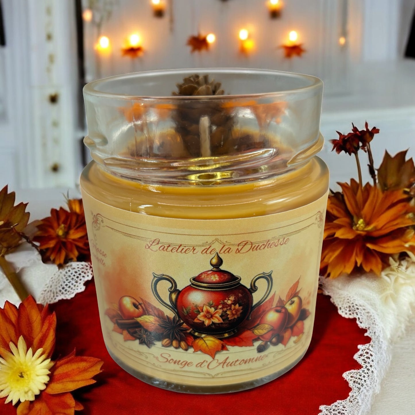 A cozy candle labeled 'Songe d'Automne' with autumn-themed design, surrounded by decorative flowers and warm lights.